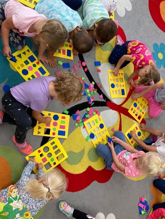 Dzieci na dywanie układają figury geometryczne