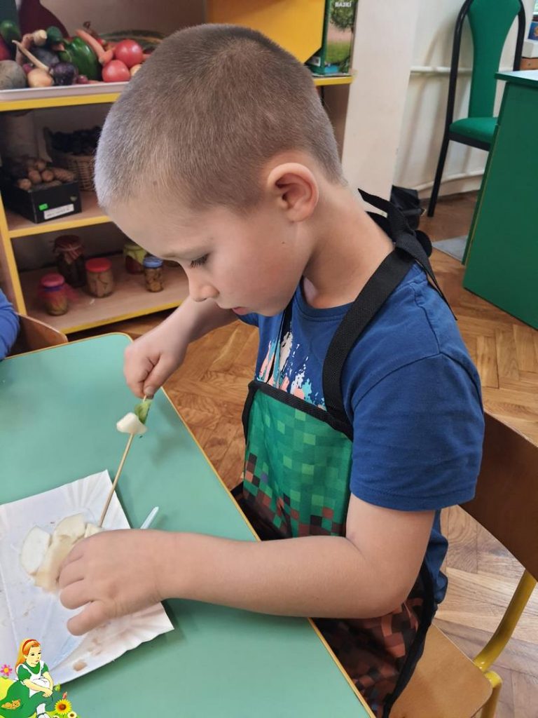 Dzieci siedzą przy stoliku i kroją owoce.